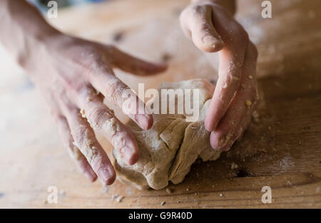 Close-up of two strong hands of a baker that are manually kneading dough on a rough, wooden kitchen table Stock Photo