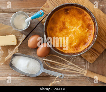 A warm cheesecake just from the oven with kitchen utensils and ingredients on a wooden table. Stock Photo