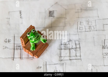 Toy frog sitting on a brick on architect sketches background Stock Photo