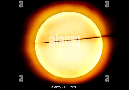 A passenger plane leaves a vapour trail as it passes in front of the sun over west London. Stock Photo