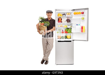 Senior man holding a bag of groceries and leaning on a refrigerator isolated on white background Stock Photo