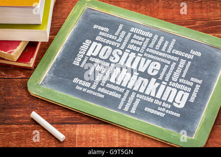 positive thinking word cloud  - white chalk text on a  slate blackboard with a stack of books against rustic wooden table Stock Photo