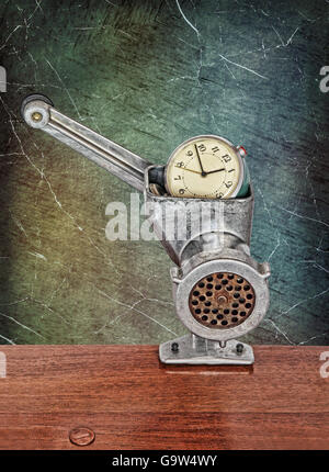 Small alarm clock in meat grinder on grunge scratched background.Toned image. Stock Photo