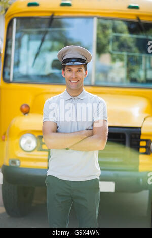 Smiling bus driver standing with arms crossed in front of bus Stock Photo