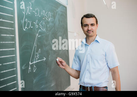 Young male teacher or student holding chalk writing on chalkboard in classroom Stock Photo