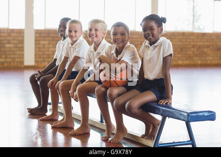 Smiling students sitting on bench with basketball Stock Photo
