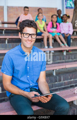 Portrait of teacher sitting on bench and using digital tablet Stock Photo