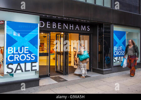 Out of focus blurred shoppers, people walking figures passing Blue Cross Summer Sale signs at Debenhams Store in Piccadilly, Manchester, UK. Sale and reductions, deals & offers, clearance items, discount, price, promotion, retail business, Everyday lifestyle street scenes outside Debenhams department store. Stock Photo