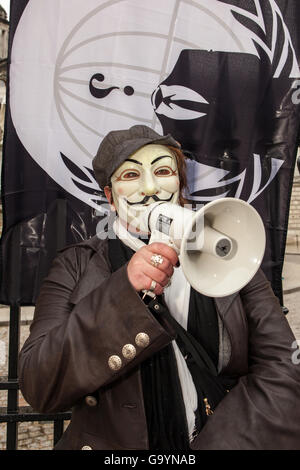 Belfast, UK, Europe. 4th July 2016. A woman wearing a Guido Fawkes/Anonymous mask with an Anonymous Flag tied to the gates of Belfast City hall where protesters staged a rally Credit:  Bonzo/Alamy Live News Stock Photo