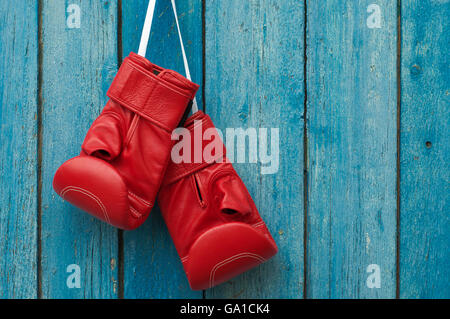 Red pair of boxing gloves hanging in a rustic blue wooden wall Stock Photo