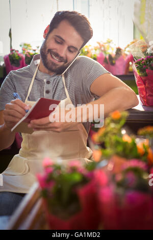 Male florist noting order in dairy while talking on mobile phone Stock Photo