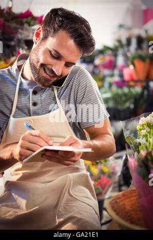 Male florist noting order in diary while talking on mobile phone Stock Photo