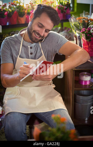 Male florist noting order in dairy while talking on mobile phone Stock Photo