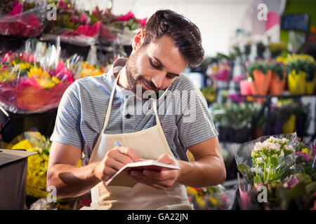 Male florist noting order in diary while talking on mobile phone Stock Photo