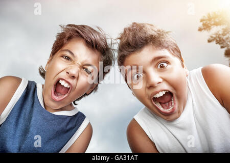 Portrait of a two crazy boys screaming to camera, over gray sky background, allow to enjoy the pleasure of freedom Stock Photo