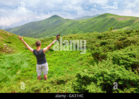 Man standing in mountains with camera raising hands Stock Photo