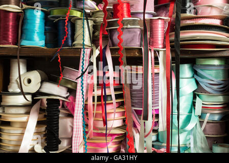 Rolls of satin ribbon tailoring supplies of different colors on wooden shelving Stock Photo