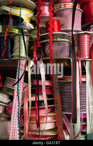 Piles of rolls of satin ribbing of different colors on wooden shelf Stock Photo