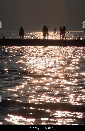 Vacationers silhouetted against reflections of setting sun on Lake Michigan; Michigan; USA Stock Photo