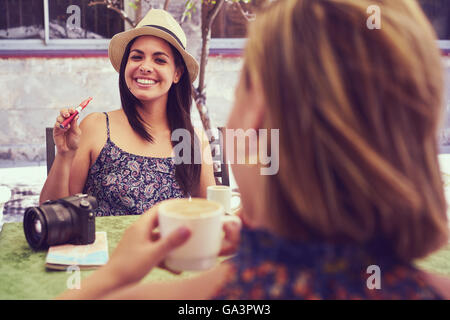 Female friends on holidays, young happy women sitting at bar smoking electronic cigarette. Stock Photo