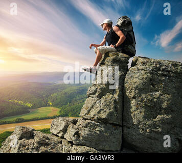 Man in mountain sitting on the cliff. Conceptual scene. Stock Photo