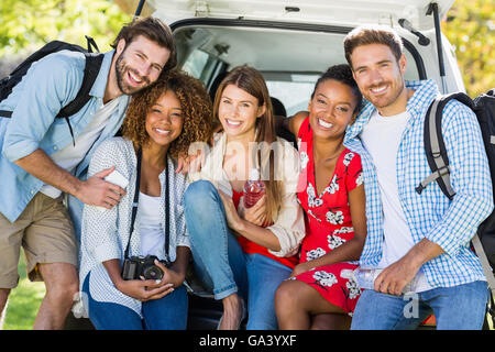 Group of friends on trip sitting in trunk of car Stock Photo