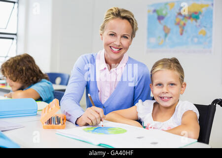 Teacher helping schoolgirl with her homework in classroom Stock Photo
