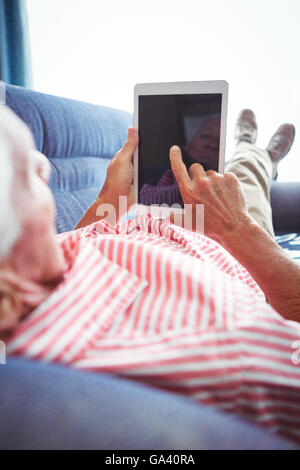 Lying on a couch senior man touching digital tablet Stock Photo