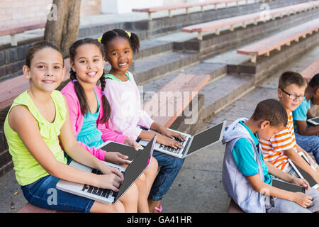 Kids sitting on bench and using laptop Stock Photo