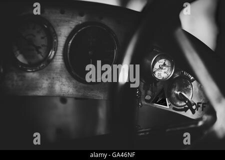 Oli pressure gauge lit up by sunlight on a vintage bugatti racing car dashboard.  Vintage monochrome filter applied Stock Photo