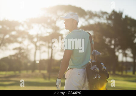 Rear view of golf player carrying bag while standing on field Stock Photo