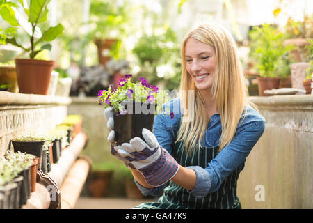 Female gardener smiling while holding flowering plant Stock Photo