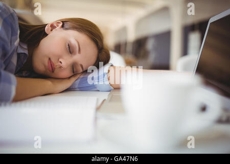 Tired businesswoman taking nap on desk in creative office Stock Photo