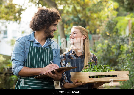 Woman holding plants in crate while gardener writing on clipboard Stock Photo