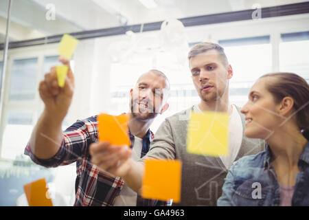 Business people sticking adhesive notes on window in office Stock Photo