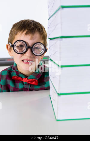 Portrait of boy by stacked books in classroom Stock Photo