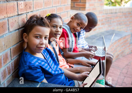 Portrait of students using digital tablet and laptop at corridor Stock Photo