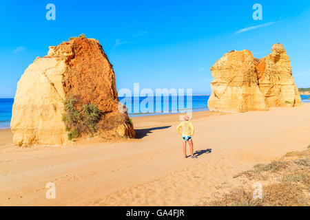 Golden colour rocks and young tourist woman standing on sandy Praia da Rocha beach, Portugal Stock Photo