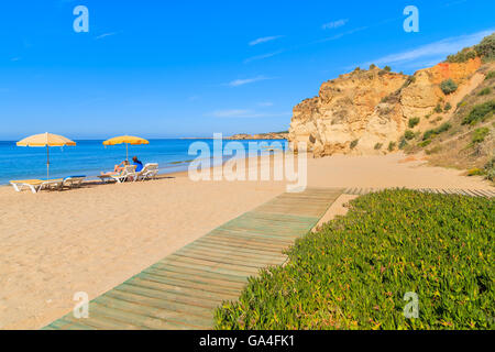 Walkway on sandy beautiful Praia da Rocha beach and two sun umbrellas in distance, Algarve region, Portugal Stock Photo