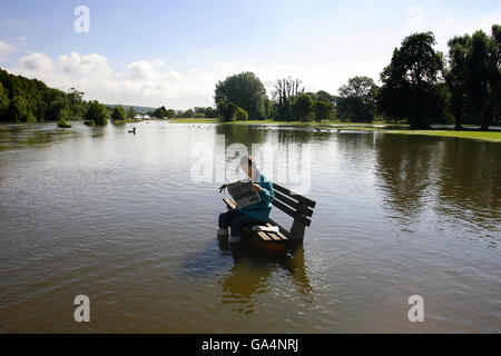 Nikki Rowlinski reads about the flooding in a newspaper as she sits beside the River Thames in Pangbourne, Berkshire where the water levels have been slowly rising today. Stock Photo