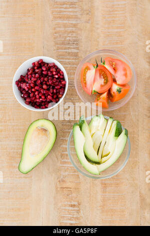 Tomato and avocado slices with pomegranate seeds in bowls on table Stock Photo