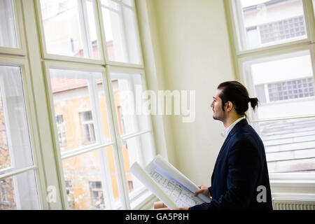 Interior designer holding blueprint while looking through window Stock Photo