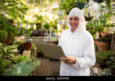Happy male scientist using laptop at greenhouse Stock Photo