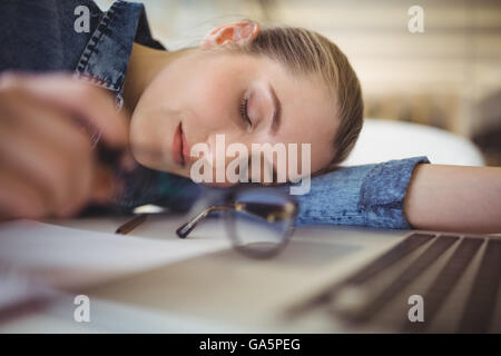 Tired businesswoman taking nap on desk in creative office Stock Photo