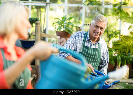 Man watering plants with woman at greenhouse Stock Photo