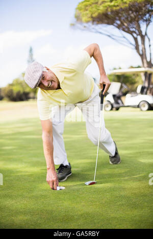 Happy mature man holding golf club while bending on grassy field Stock Photo