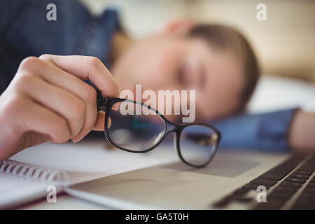 Tired businesswoman holding eyeglasses while taking nap in office Stock Photo