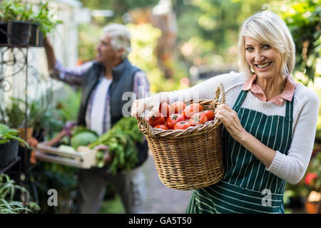 Female gardener carrying tomatoes in wicker basket Stock Photo