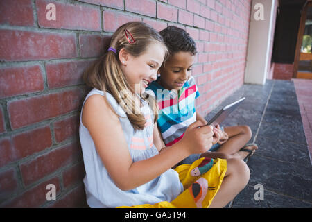 Schoolkids sitting in corridor and using digital tablets Stock Photo