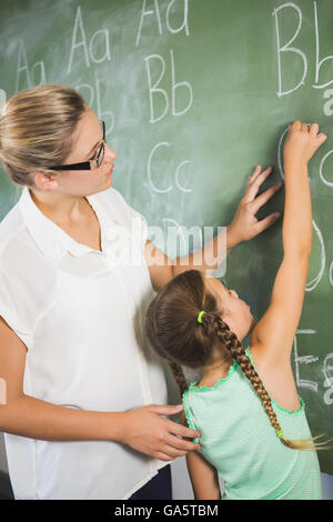 Teacher assisting schoolgirl to learn alphabet on chalkboard in classroom Stock Photo